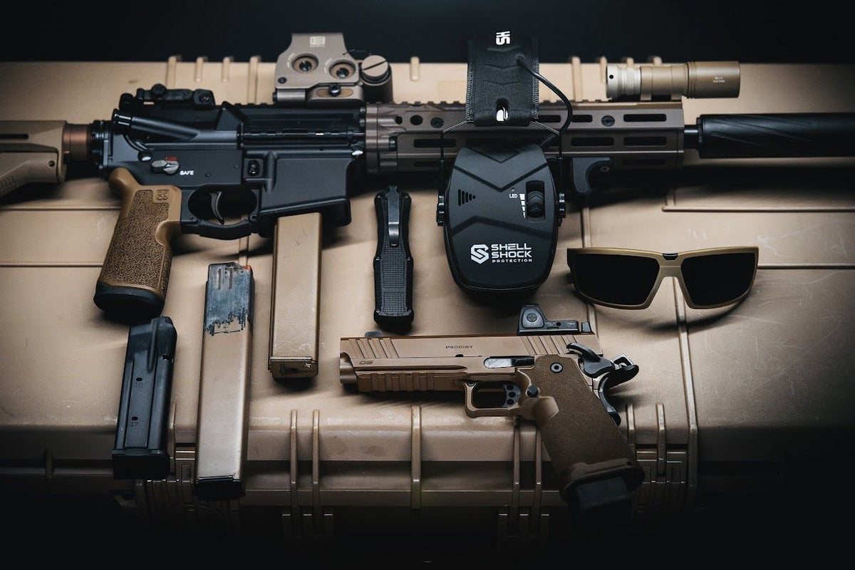 ShellShock Protection earmuffs and shooting glasses on a tan range case with a rifle, pistol, magazines, and a knife.