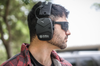 Man wearing EXO Pro Elite earmuffs and Eclipse sunglasses outdoors, side profile showing battery compartment.