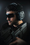 Shooter wearing EXO Pro Elite electronic earmuffs and SWITCH ballistic glasses, low-light studio shot